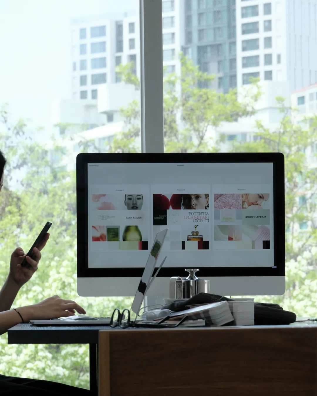 A studio desk with a monitor showing project layouts by a window